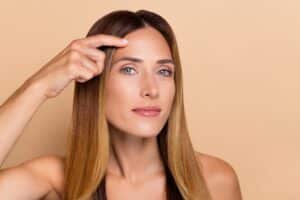 Smiling woman framing her forehead and brow area with her hands.