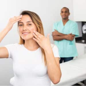 Portrait of happy smiling Latin American woman client of professional esthetician after facelift procedure, man doctor on background