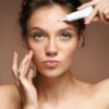 girl with problem skin applying treatment cream on beige background
