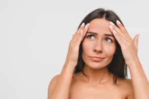Woman looking at forehead wrinkles, considering a forehead lift.